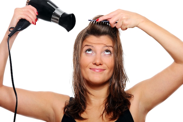 Una joven mujer bonita secándose y cepillando su cabello sobre fondo blanco.