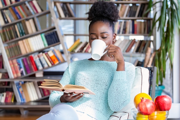 Joven mujer bonita sentada y bebiendo café mientras lee un libro