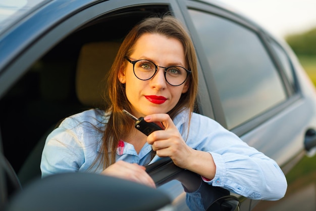 Foto joven mujer bonita sentada en un coche con las llaves en la mano concepto de comprar un coche usado o un coche de alquiler