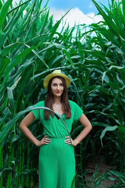 Foto joven mujer bonita con el sombrero amarillo entre las plantas de maíz en el campo de maíz durante la temporada de verano