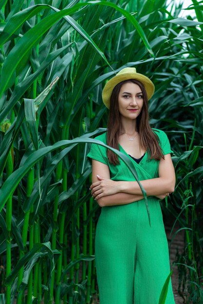 Joven mujer bonita con el sombrero amarillo entre las plantas de maíz en el campo de maíz durante la temporada de verano