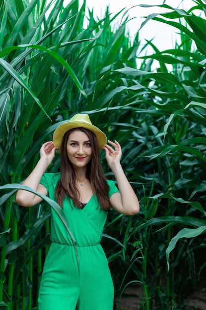 Joven mujer bonita con el sombrero amarillo entre las plantas de maíz en el campo de maíz durante la temporada de verano