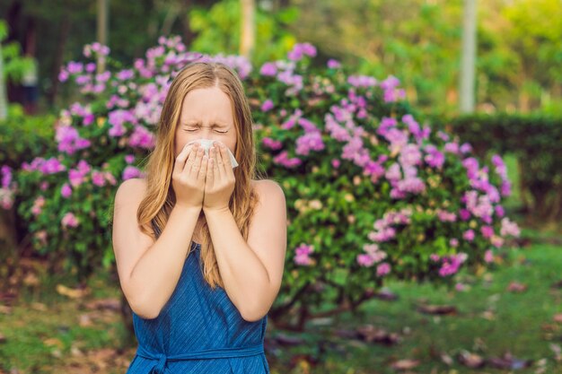 Joven mujer bonita sonarse la nariz frente a un árbol floreciente Concepto de alergia primaveral