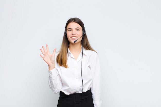 Joven mujer bonita sonriendo y mirando amigable, mostrando el número cinco o quinto con la mano hacia adelante, contando con auriculares y micrófono