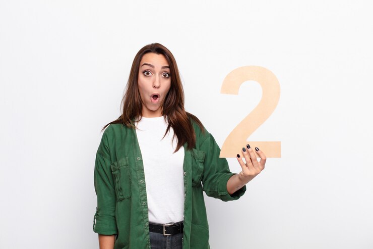Foto joven mujer bonita sorprendida, sorprendida, asombrada, sosteniendo un número 2
