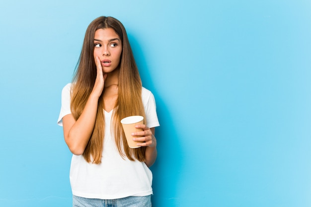 Joven mujer bonita sosteniendo un café para llevar está diciendo una noticia secreta de frenado en caliente y mirando a un lado