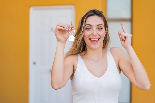 Joven mujer bonita sosteniendo las llaves de la casa al aire libre señalando una gran idea