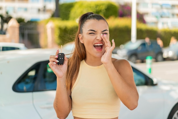 Joven mujer bonita sosteniendo las llaves del coche al aire libre gritando con la boca abierta