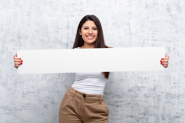 Joven mujer bonita sosteniendo una pancarta contra la pared del grunge