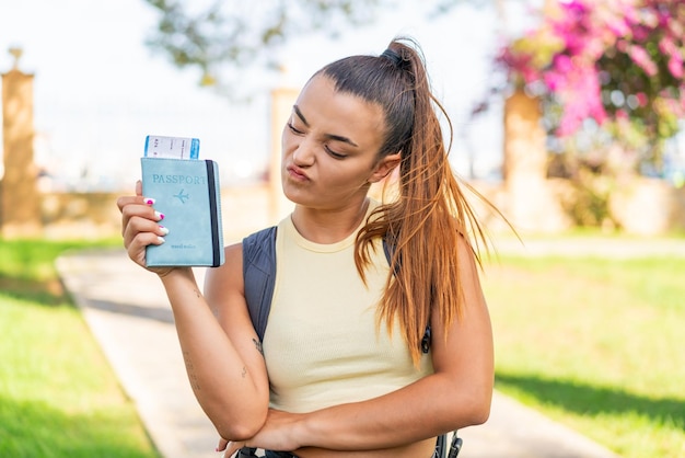 Foto joven mujer bonita sosteniendo un pasaporte al aire libre con expresión triste