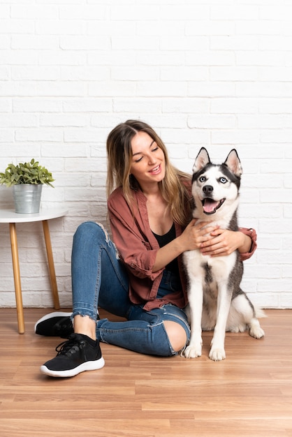 Joven mujer bonita con su perro husky sentado en el suelo en el interior