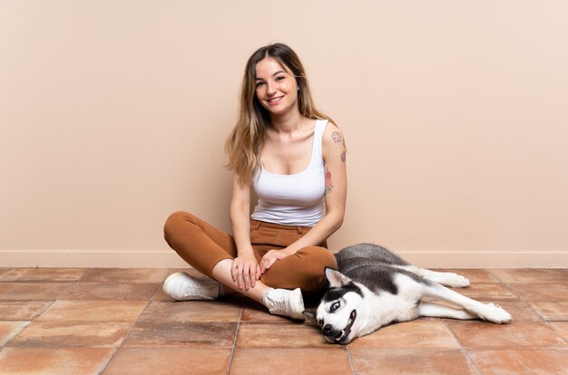 Joven mujer bonita con su perro husky sentado en el suelo en el interior