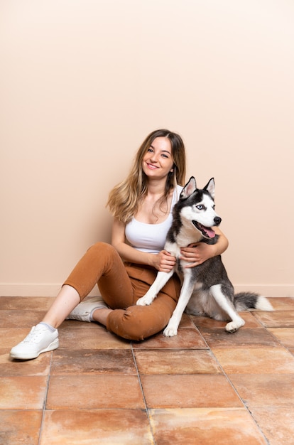 Joven mujer bonita con su perro husky sentado en el suelo en el interior