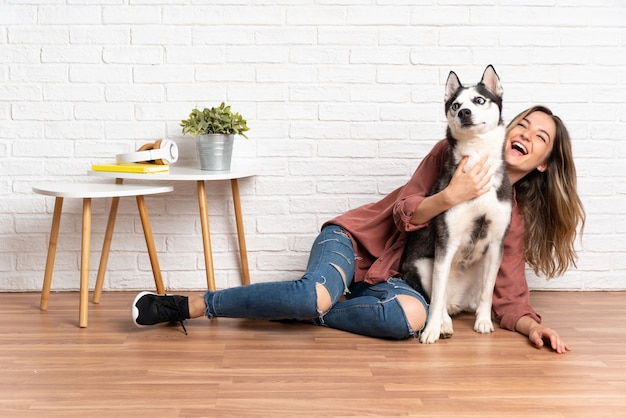 Joven mujer bonita con su perro husky sentado en el suelo en el interior