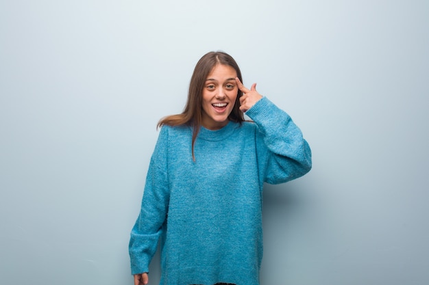 Joven mujer bonita con un suéter azul haciendo un gesto de decepción con el dedo