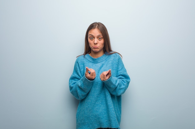 Joven mujer bonita con un suéter azul haciendo un gesto de necesidad