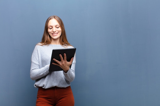 Joven mujer bonita con una tableta en la pared azul con un espacio de copia