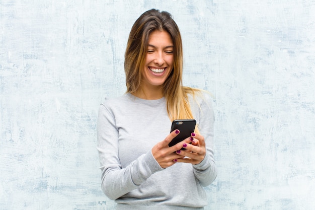 Joven mujer bonita con un teléfono inteligente contra la pared del grunge