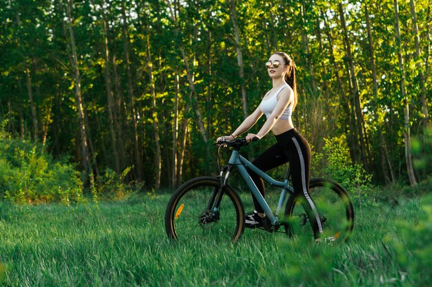 Joven mujer bonita tiene un paseo en bicicleta en un parque al atardecer