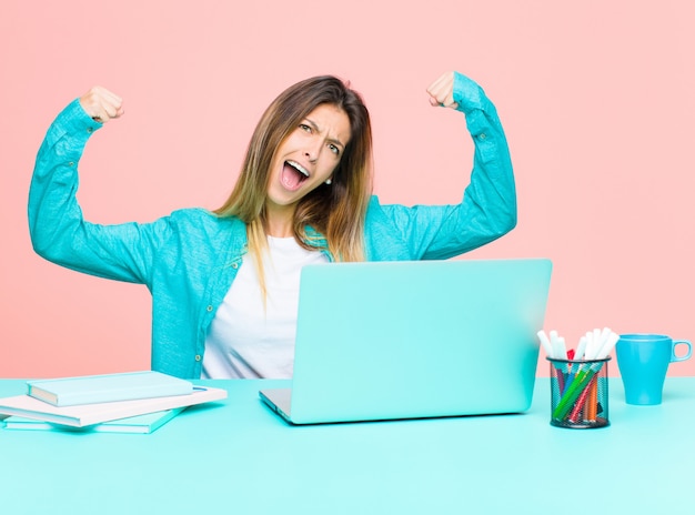 Joven mujer bonita trabajando con una computadora portátil gritando triunfante, luciendo emocionada, feliz y sorprendida ganadora, celebrando