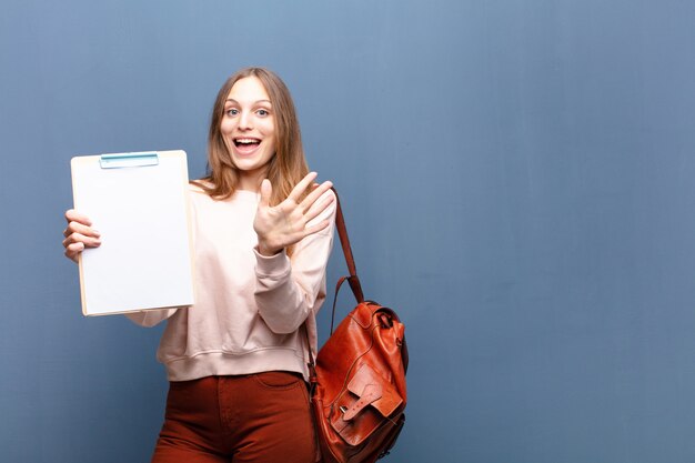 Joven mujer bonita con un trozo de papel contra la pared azul con un copyspace