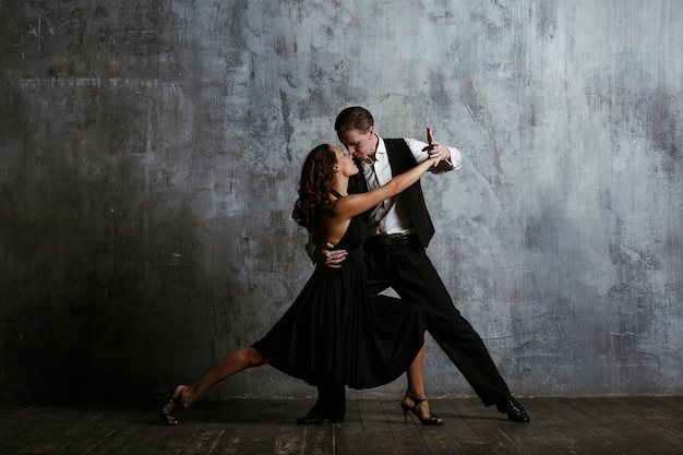 Joven mujer bonita en vestido negro y hombre baila tango