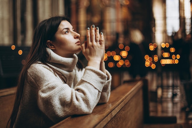 Una joven mujer bonita vino al templo a orar a Dios La feligresa de la iglesia se sienta en un banco con las manos cruzadas para orar y reza de todo corazón copia espacio
