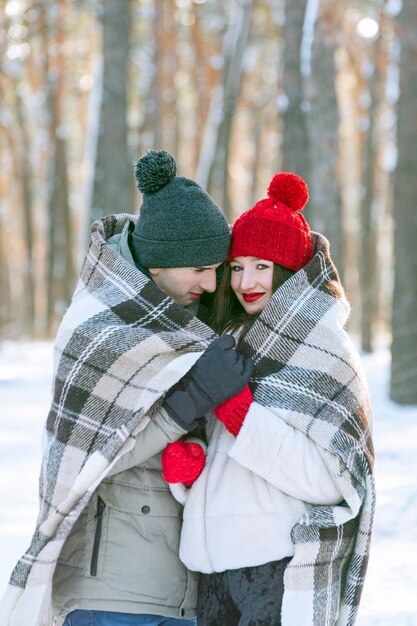 Un joven y una mujer en un bosque invernal cubierto de nieve se cubrieron con una manta cálida. Marco vertical.