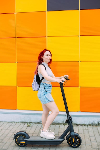 Joven mujer brillante sonríe y monta un scooter eléctrico en el verano en la ciudad