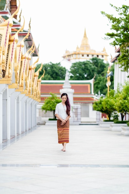 Joven mujer budista asiática con traje tradicional de Tailandia se para en la iglesia para relajarse y meditar Santuario Ratchanatdaram bangkok