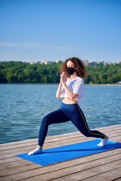 Una joven mujer con cabello rizado haciendo yoga afuera