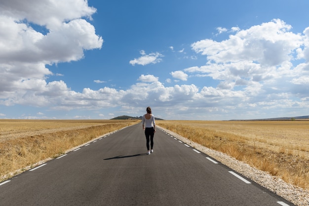 Joven mujer caminando en el camino con cielo nublado.