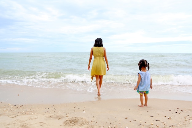 Joven mujer caminando directamente al mar y su niña de pie en la playa