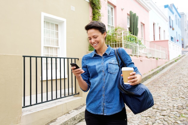 Joven mujer caminando con teléfono móvil y bolso fuera