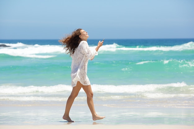 Joven mujer caminando con teléfono móvil en la playa