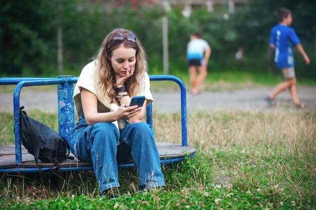 Joven mujer cansada frustrada sentada en el patio de recreo y mirando su teléfono