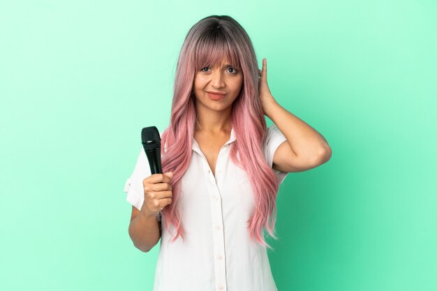 Joven mujer cantante de raza mixta con cabello rosado aislado sobre fondo verde con dudas