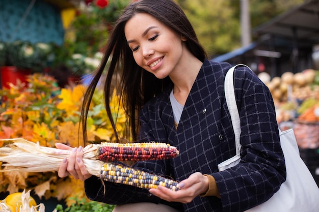 Joven mujer casual atractiva comprando alegremente maíz colorido en la tienda de otoño al aire libre
