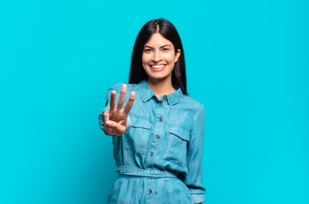 Foto joven mujer casual hispana sonriendo y mirando amistosamente, mostrando el número tres o tercero con la mano hacia adelante, contando hacia atrás