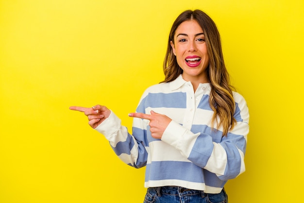 Joven mujer caucásica aislada en amarillo apuntando con los dedos índices a un espacio de copia, expresando entusiasmo y deseo.