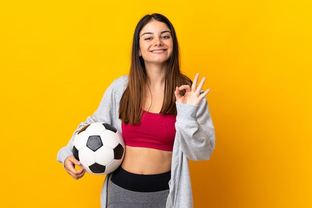 Joven mujer caucásica aislada en amarillo con balón de fútbol y haciendo aceptar firmar