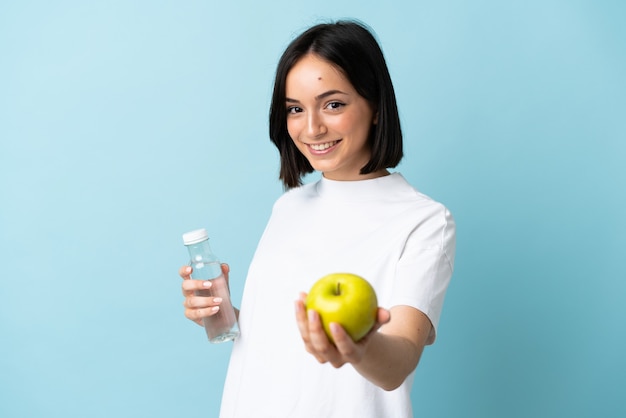 Joven mujer caucásica aislada en azul con una manzana y con una botella de agua