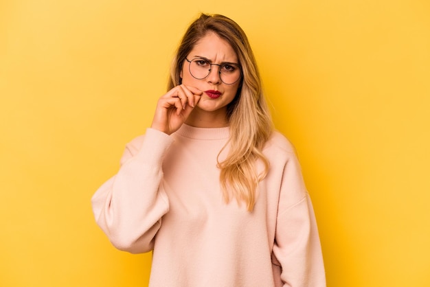 Joven mujer caucásica aislada de fondo amarillo con los dedos en los labios guardando un secreto