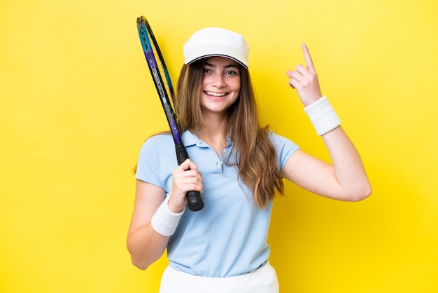 Joven mujer caucásica aislada en fondo amarillo jugando al tenis y apuntando hacia arriba