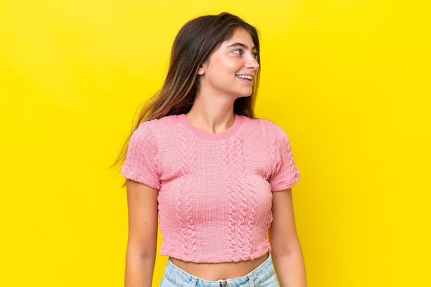 Joven mujer caucásica aislada en fondo amarillo mirando hacia el lado