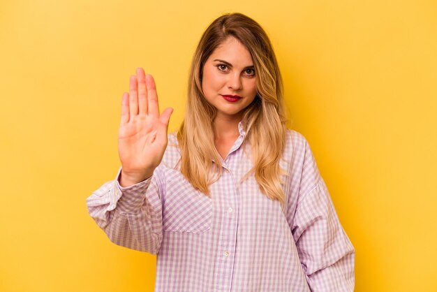 Joven mujer caucásica aislada de fondo amarillo parada con la mano extendida mostrando la señal de stop que te impide