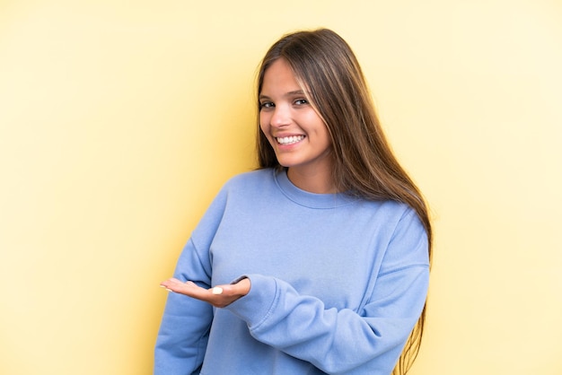 Joven mujer caucásica aislada de fondo amarillo que presenta una idea mientras mira sonriendo hacia