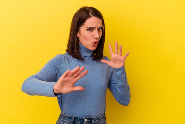 Joven mujer caucásica aislada de fondo amarillo rechazando a alguien mostrando un gesto de disgusto