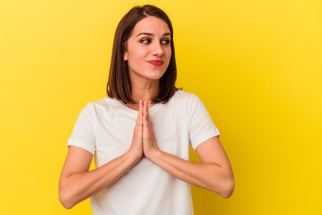 Joven mujer caucásica aislada de fondo amarillo rezando mostrando devoción persona religiosa en busca de inspiración divina