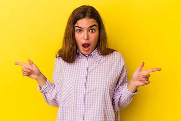 Joven mujer caucásica aislada de fondo amarillo señalando diferentes espacios de copia, eligiendo uno de ellos, mostrando con el dedo.
